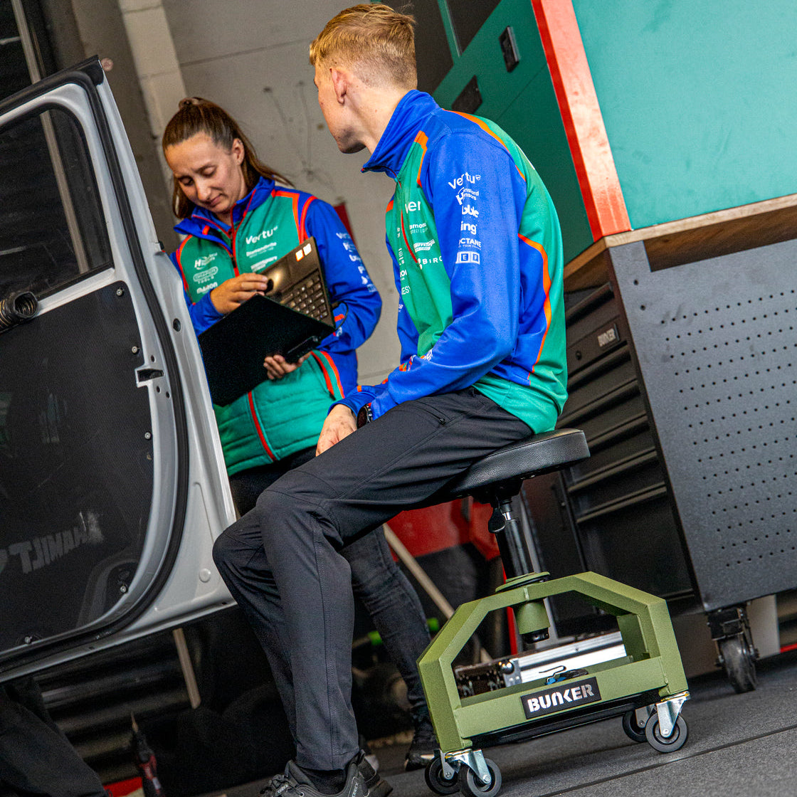 man sitting on the BUNKER Adjustable Work Stool with another team member
