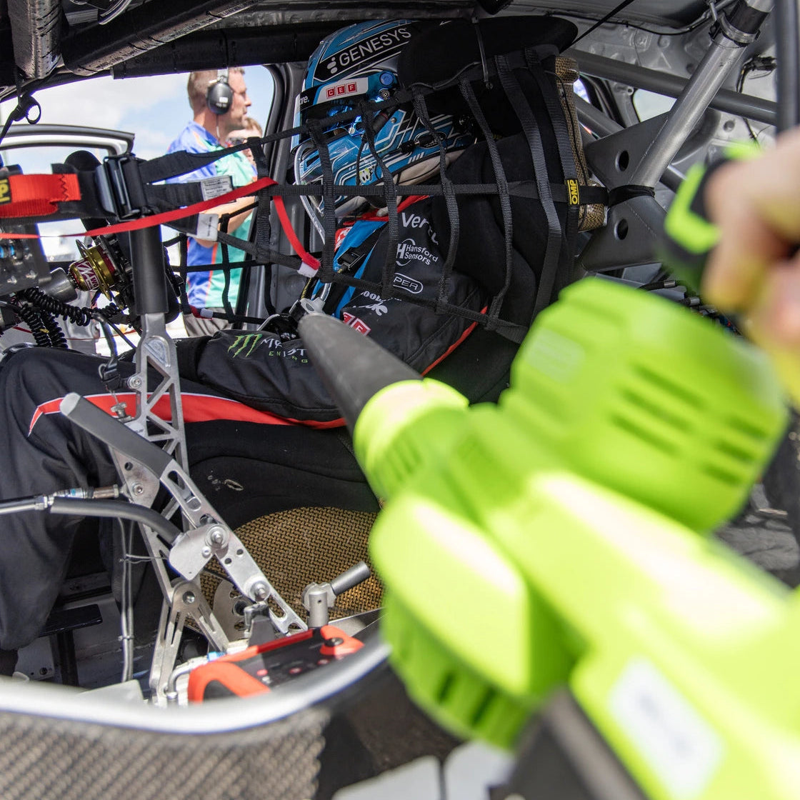 A close-up action shot inside a race car cockpit with a leaf blower in use