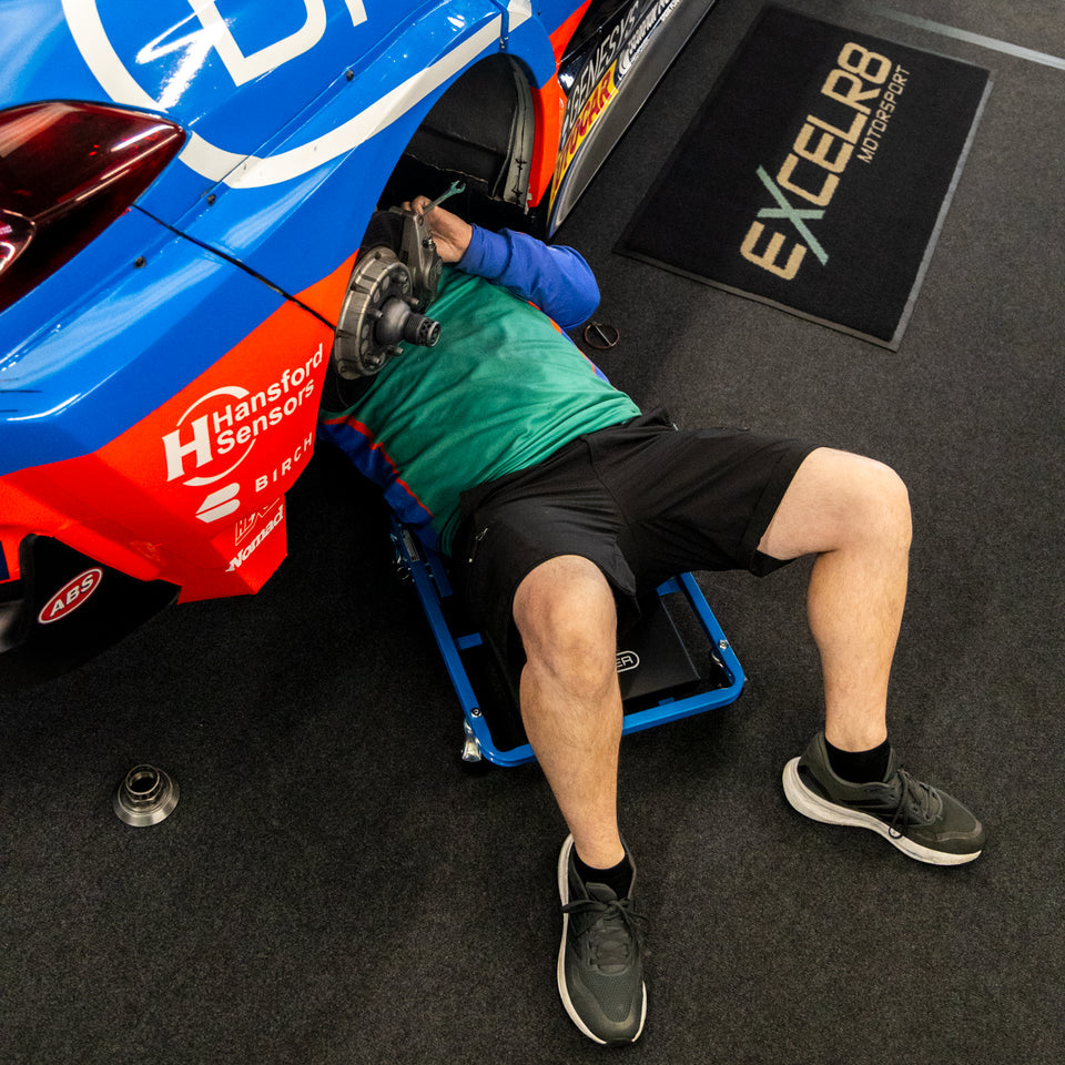 A race car pit crew member under the EXCELR8 car using the Car Creeper & Seat by Draper tools