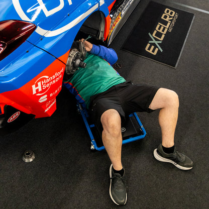 A race car pit crew member under the EXCELR8 car using the Car Creeper & Seat by Draper tools