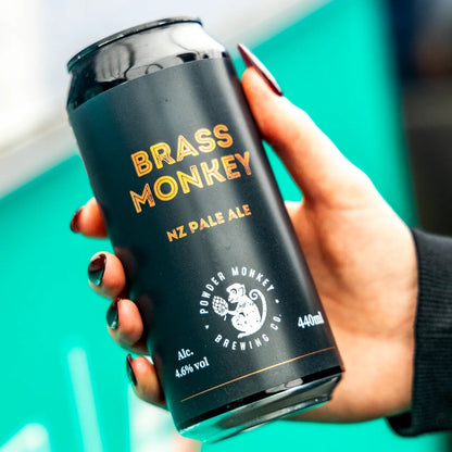 A hand with dark red nail polish holds a black can of Brass Monkey NZ Pale Ale. 