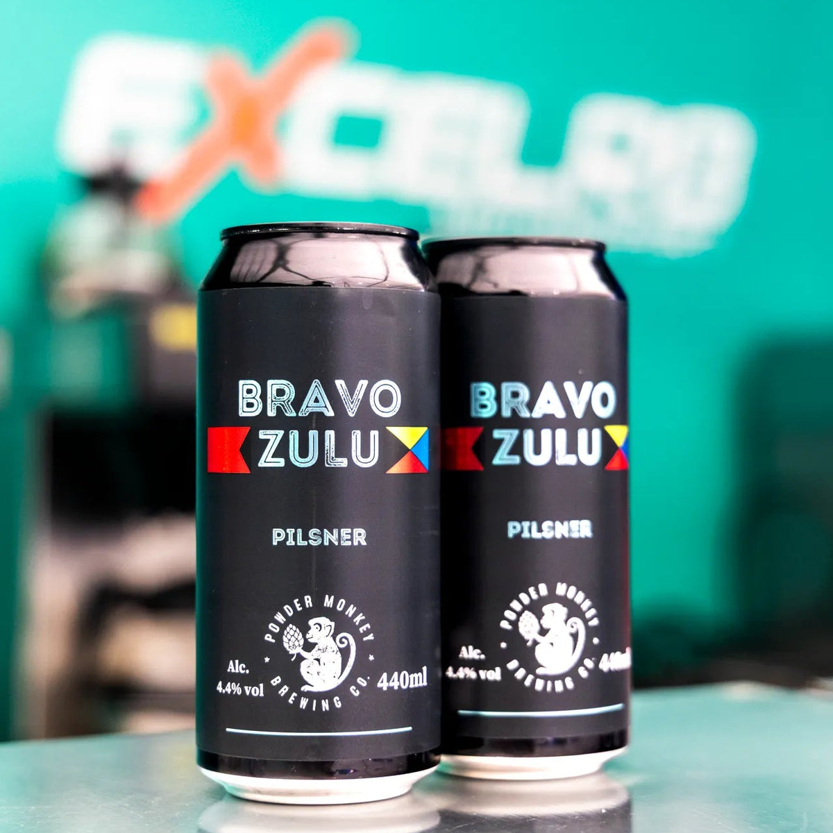 2 Cans of Bravo Zulu Infront of the EXCLER8 Logo