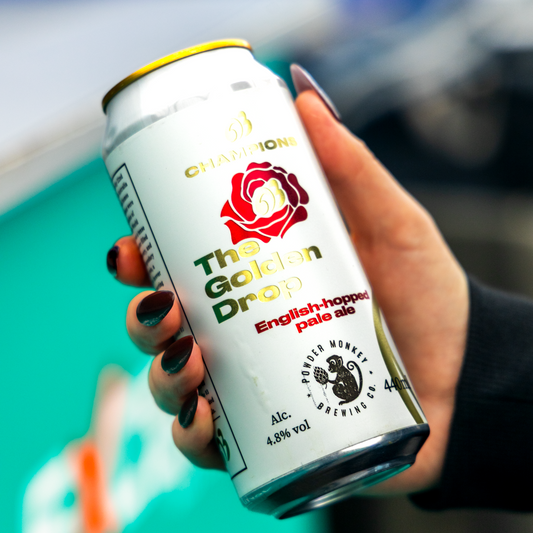 A hand with dark nail polish holds a can of Champion The Golden Drop