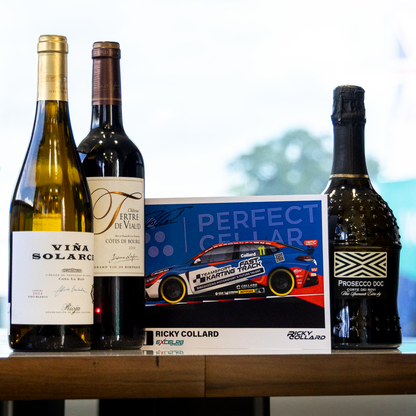 A collection of gourmet beverages arranged on a wooden table, featuring a bottle of Vira Solari white wine, a bottle of Valtori wine, a Proton Drive sparkling wine bottle, and a race card for Ricky Collard.